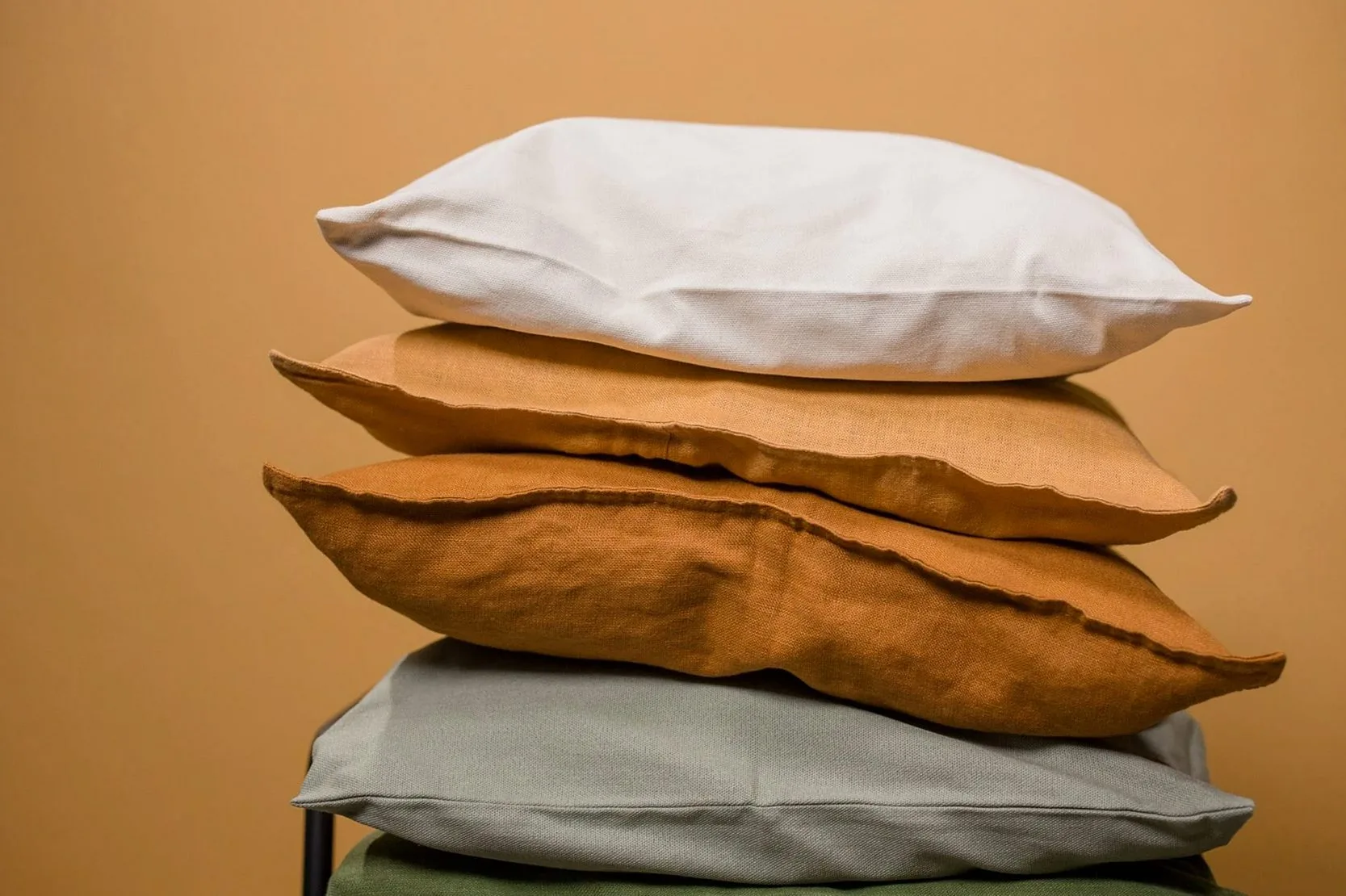 Stack of different colorful pillows folded and placed in stack on chair isolated on dark beige background