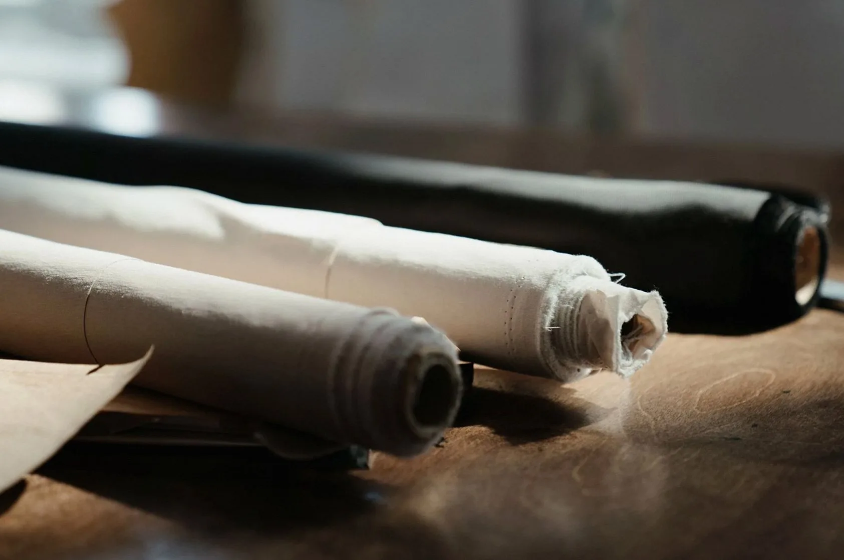 Detailed view of fabric rolls on a wooden table in an artisan workshop, capturing texture and craftsmanship.